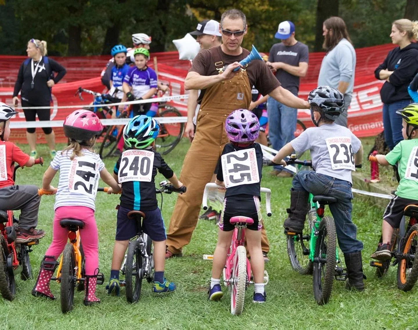 The start line of a junior race, official is holding a horn in his hand with the young racers looking up at him.
