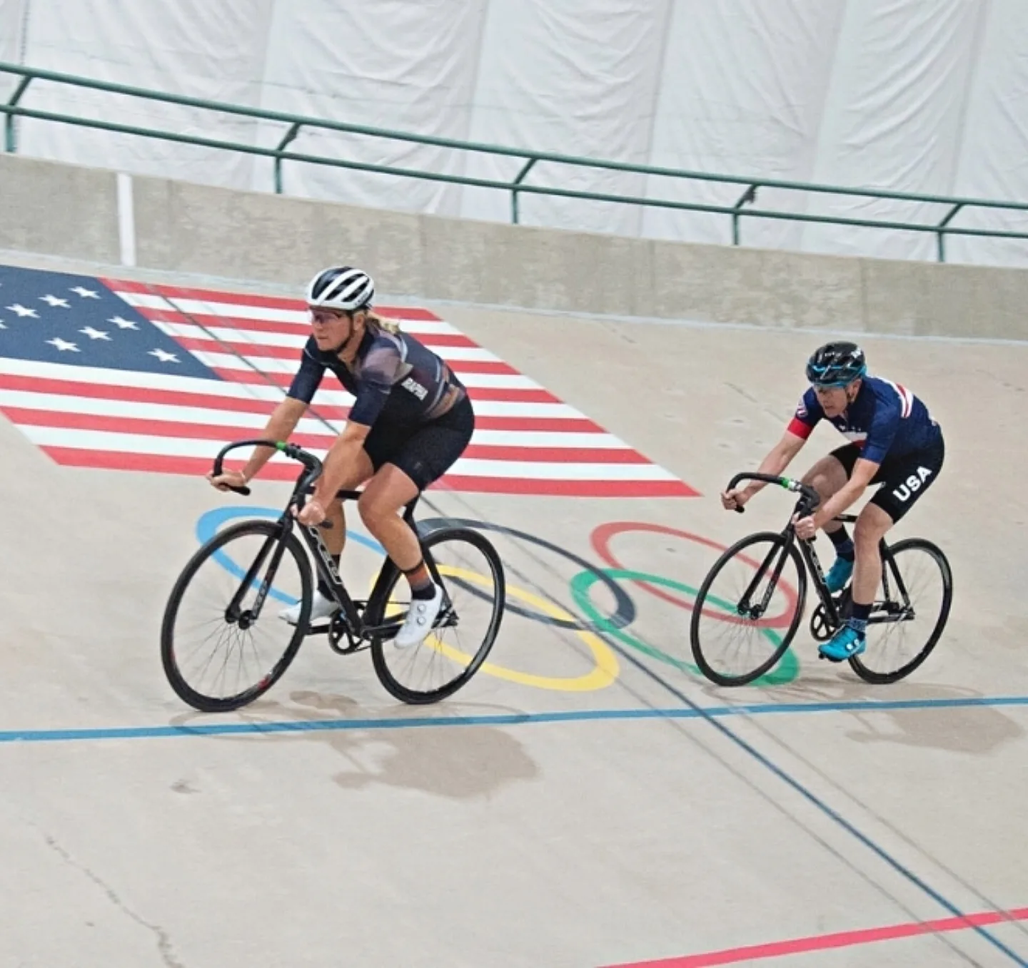 Two track cyclists riding in a velodrome.