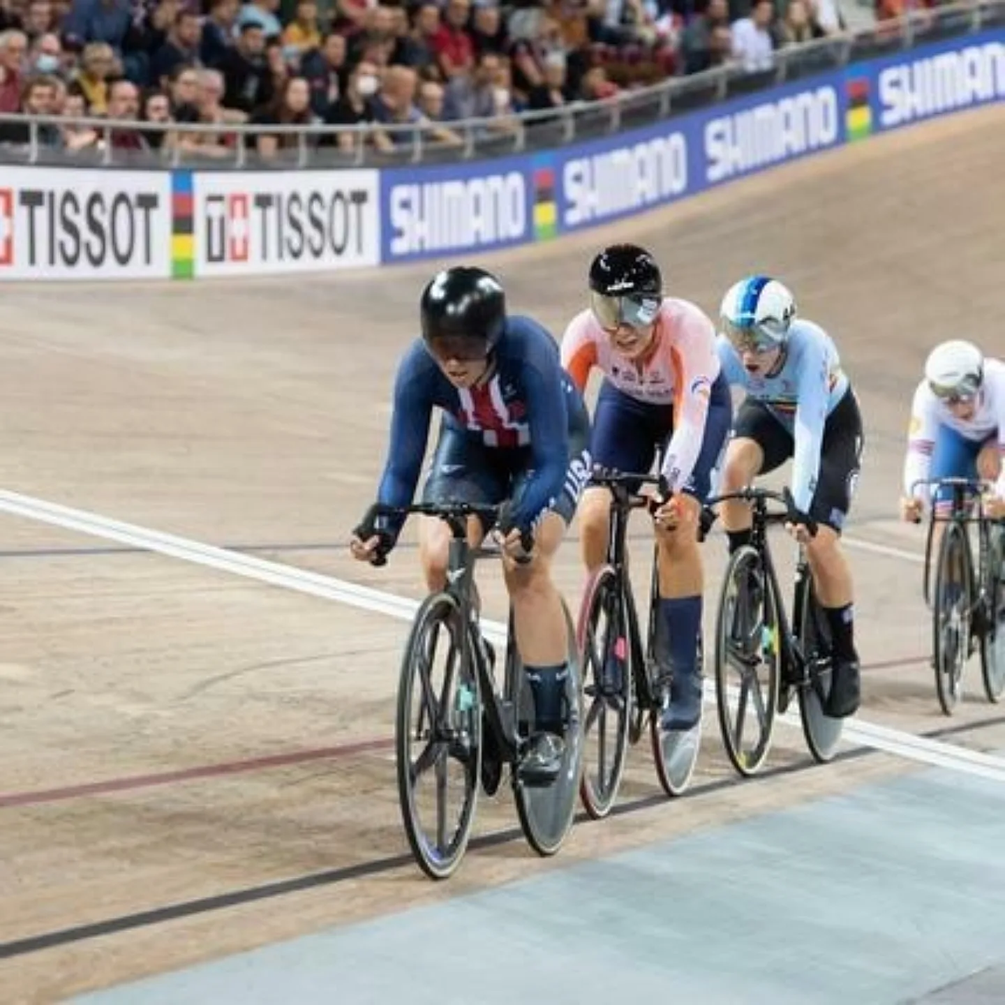 Group of track racers with USA in the lead racing in a velodrome.