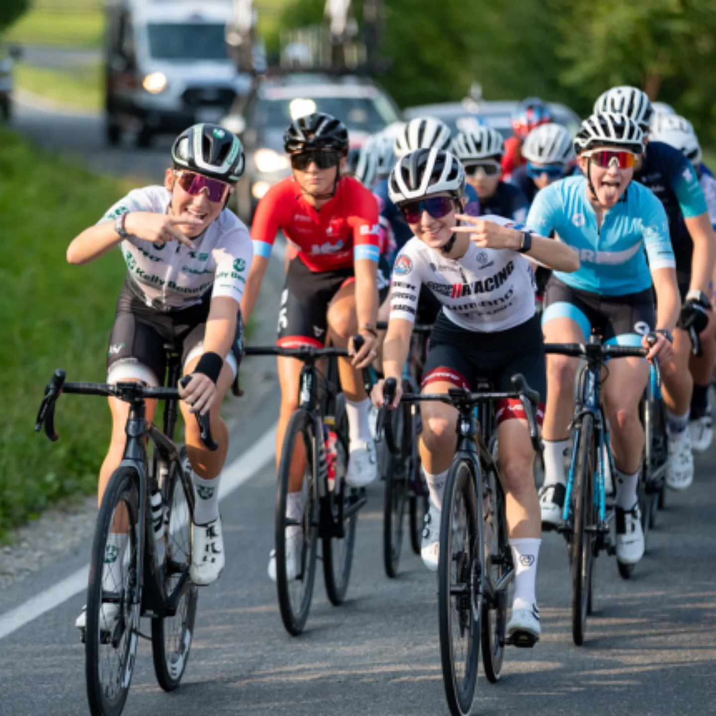 Two team bike racers giving the peace sign while leading a pack of bike racers