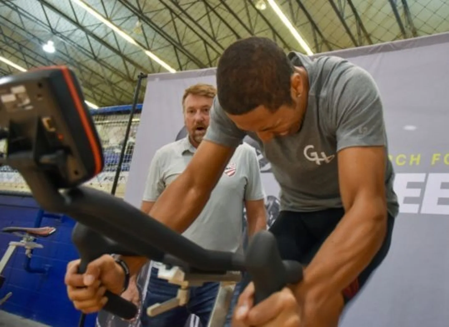 Man riding a watt bike, he is working very hard and gripping in the drop handlebars.