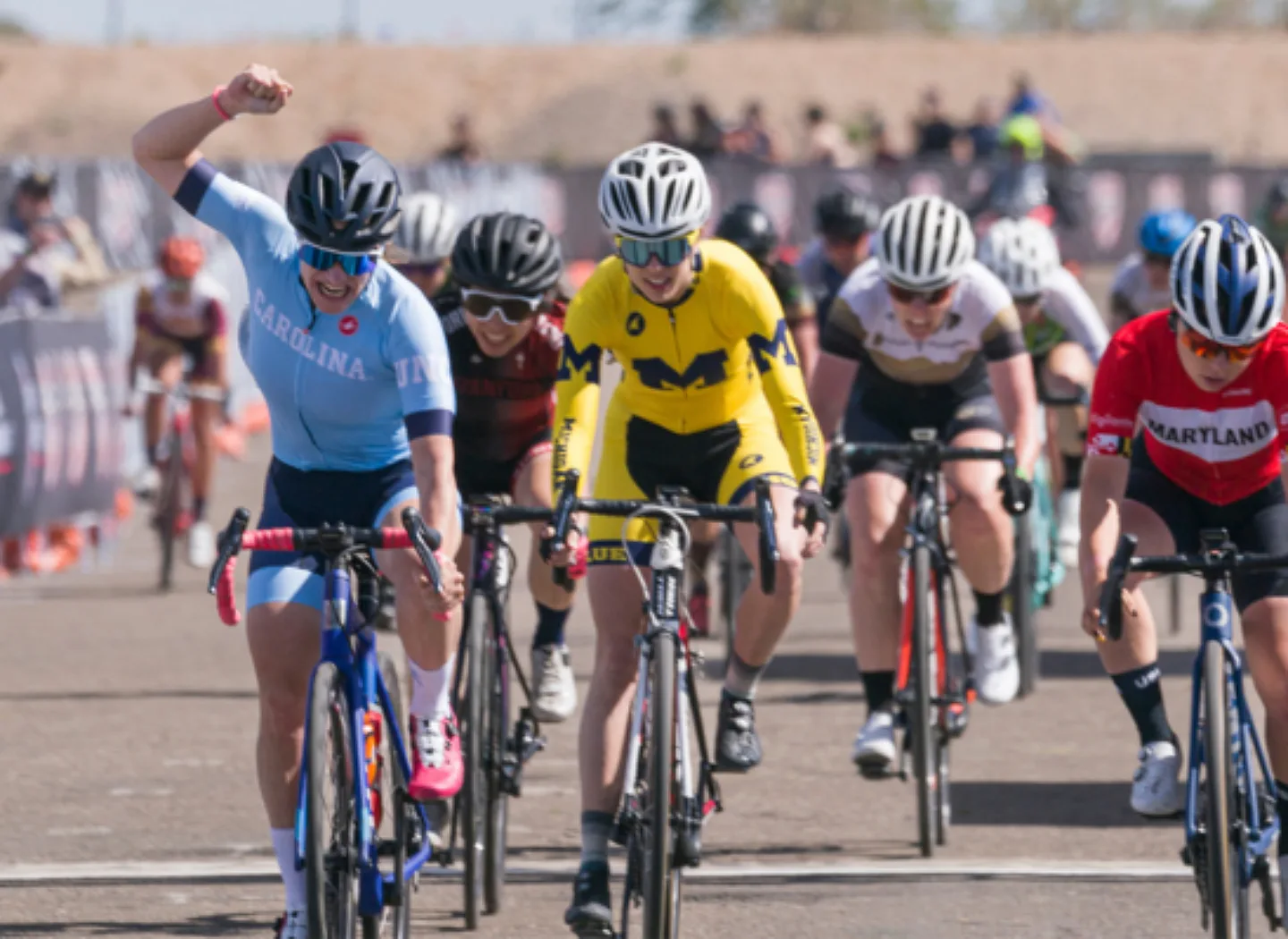 Collegiate female celebrating winning a road race while still on her bike.