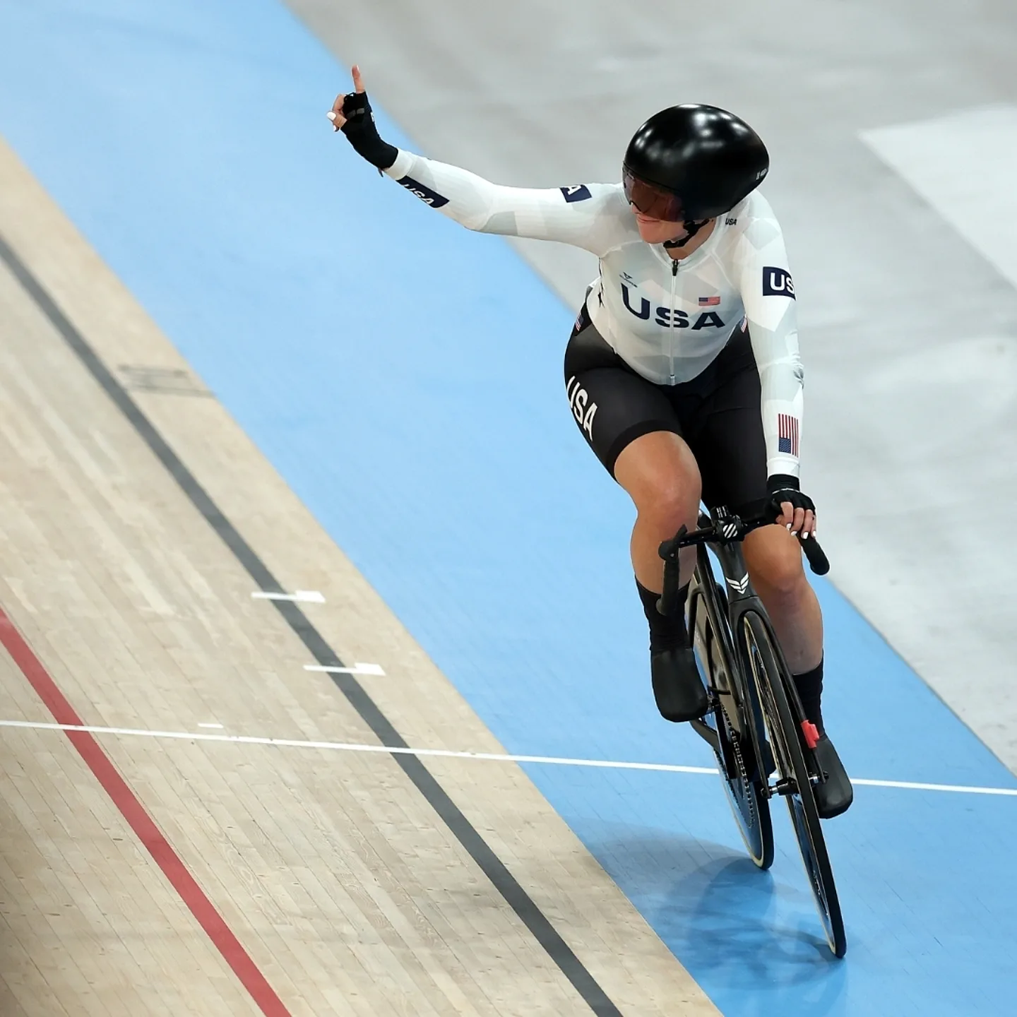 Team USA track cyclist holding one finger in the air to celebrate her win.