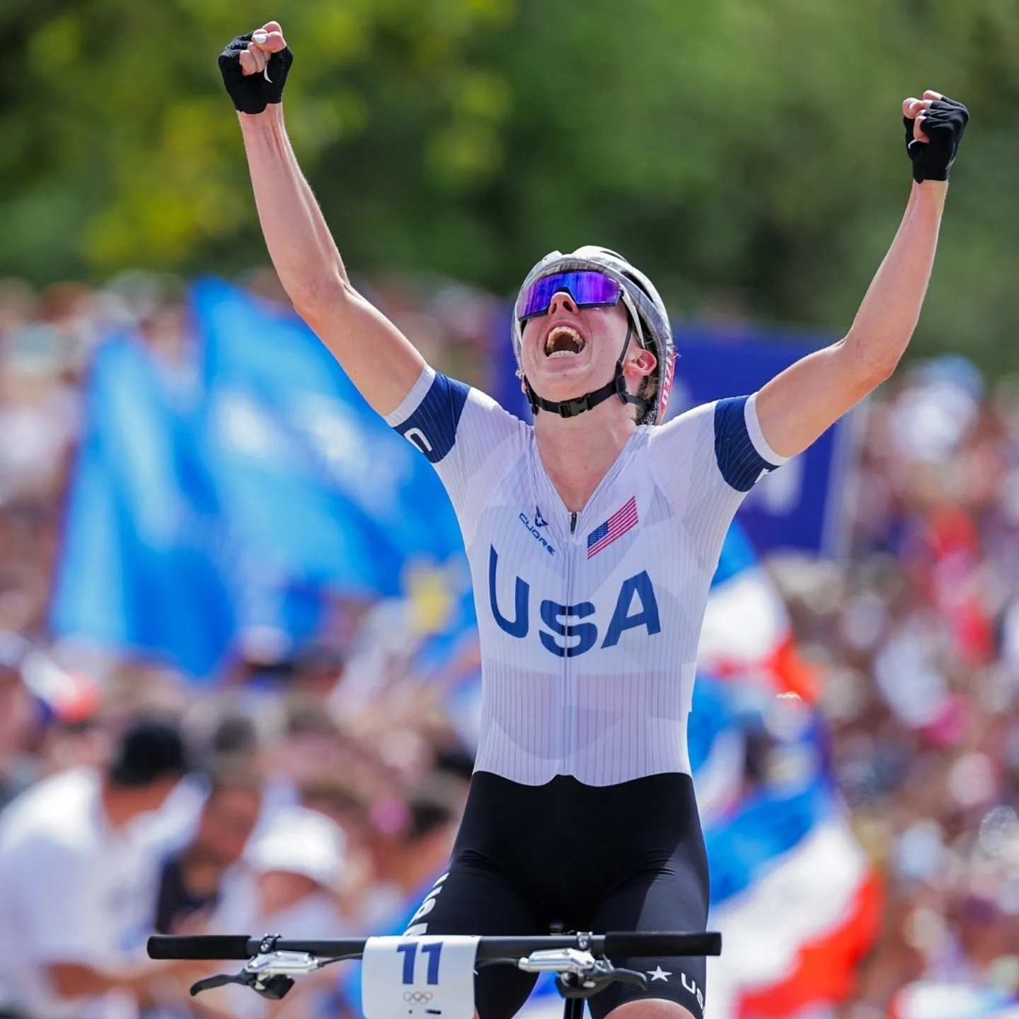 Haley Batten celebrating her silver medal with both hands in the air off of her bike.
