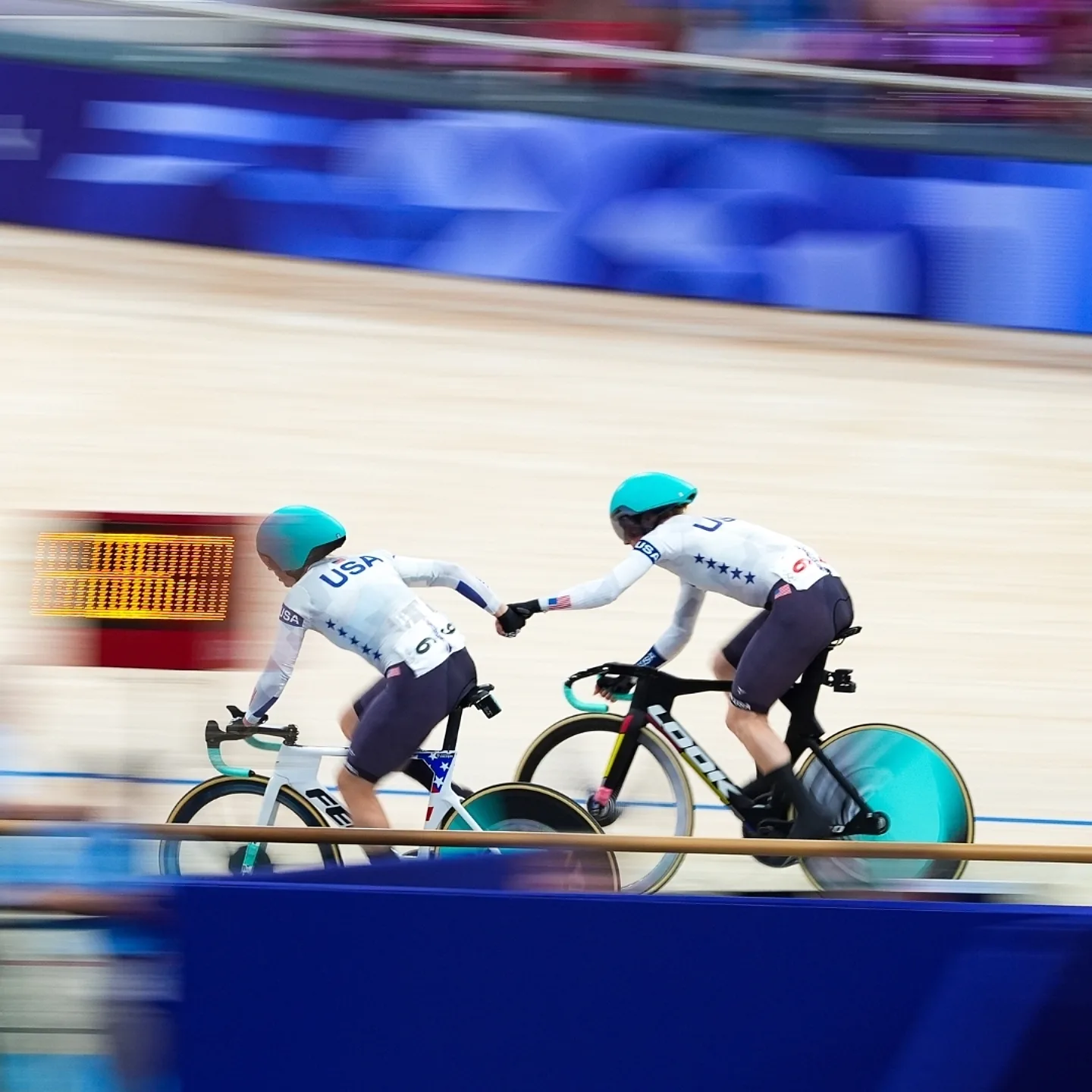 Two track cyclists performing a hand sling exchange, in the Madison event in track cycling.