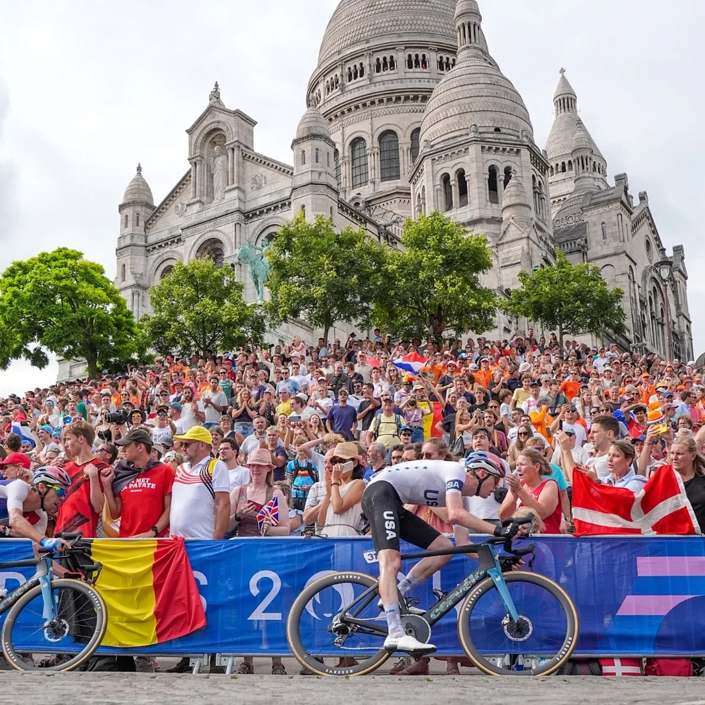 Team USA athlete going through a corner during a road race while being cheered on by fans.