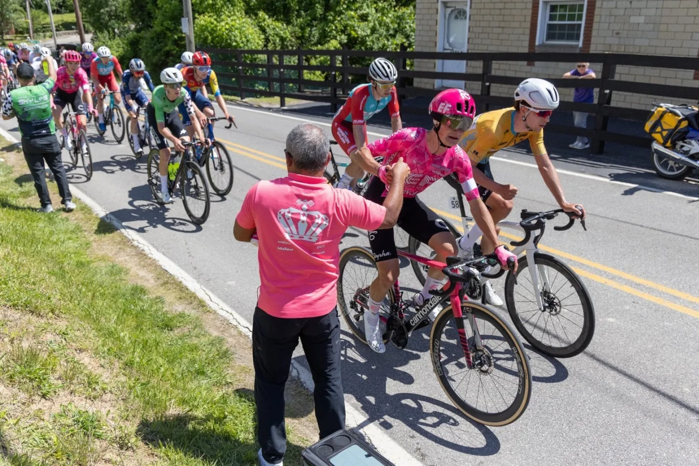 USA Cycling support crew member assisting a cyclist with a water bottle during a road race